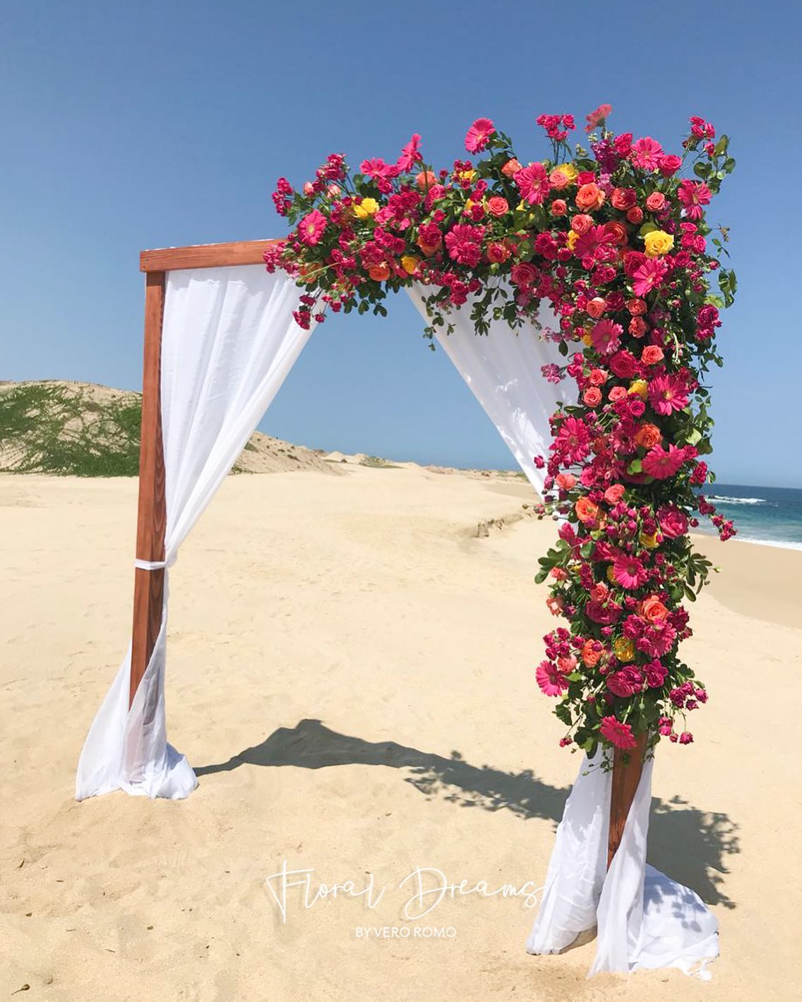 wooden wedding arch on beach with large hot pink flower arrangement attached