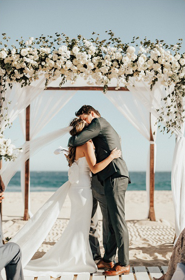 bride and first kiss in beach wedding under large floral arch