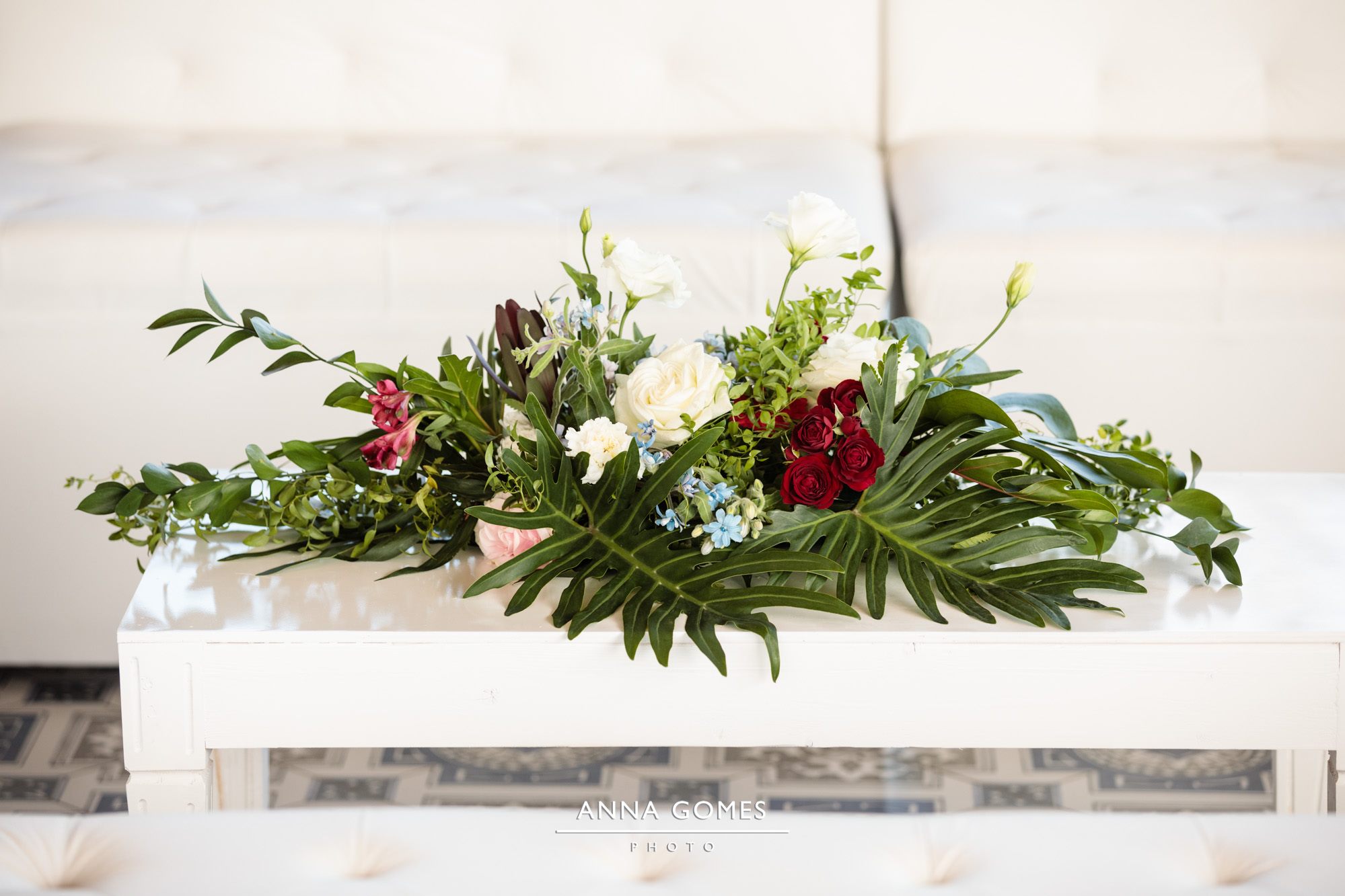 white and burgundy flower arrangement with tropical leaves