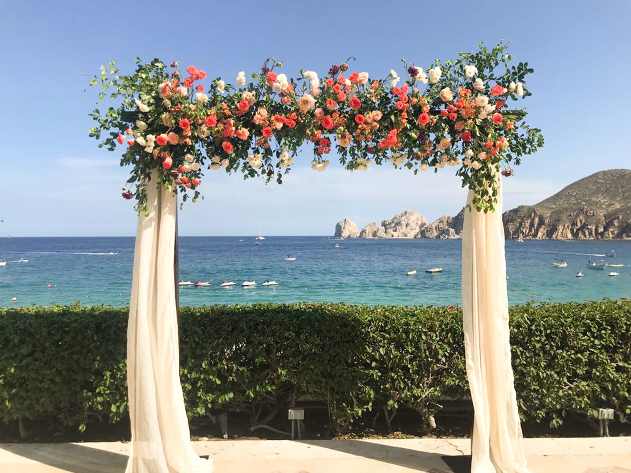 wedding arch with pink flowers in front of blue ocean